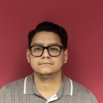 Man with glasses against a pink background.